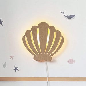 Könnte beinhalten: Ein Nachtlicht aus Holz in Form einer Muschel mit warmem Schein. Die Muschel ist ausgeschnitten und hat ein Kabel zum Anschließen.