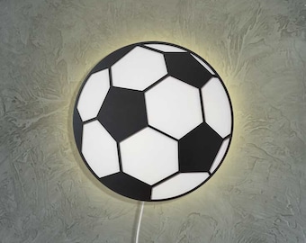 May include: A black and white soccer ball shaped wall light. The light is illuminated and casts a warm glow.