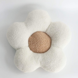 Puede incluir: Una almohada de felpa blanca con forma de flor con un centro marrón. La almohada es suave y esponjosa y sería perfecta para agregar un toque de fantasía a cualquier habitación.