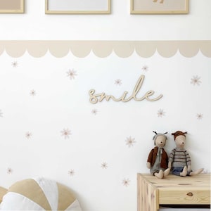May include: A white wall with a beige scalloped border and a wooden sign that says "smile". There are small pink flower decals scattered across the wall. Two plush toys are sitting on a wooden shelf.