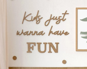 May include: Wooden wall decor featuring the text "Kids just wanna have FUN" in a light brown colour. The letters are arranged in a playful, whimsical style. Small brown circles are scattered around the letters, adding a touch of whimsy to the design.