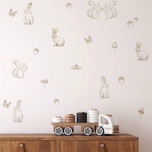 May include: A white wall with brown animal and nature themed wall decals. The decals include rabbits, squirrels, butterflies, acorns, and mushrooms.
