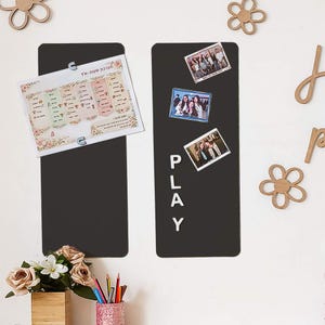 Può includere: Due lavagne magnetiche rettangolari nere con foto e un foglio di carta. Una lavagna ha la parola "PLAY" in bianco. L'altra lavagna ha un foglio di carta con testo e un motivo floreale. Ritagli di fiori e lettere in legno sono sparsi.