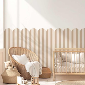 Puede incluir: Un interior de guardería con una cuna de madera clara, una silla de mimbre y una pared a rayas. La silla tiene una almohada y una manta blancas. Cestas tejidas contienen juguetes. La pared presenta rayas verticales beige y blancas.