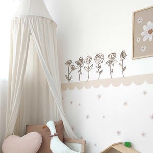 May include: A white canopy bed with a wooden frame and a white fabric canopy. The wall behind the bed is decorated with a row of wooden flower cutouts and a small framed print of flowers.