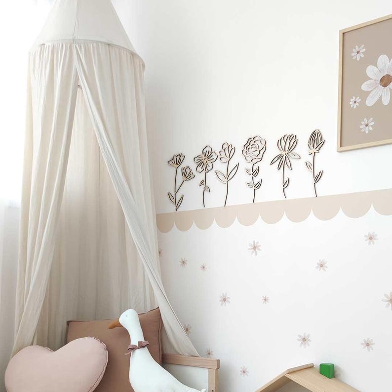 May include: A white canopy bed with a wooden frame and a white fabric canopy. The wall behind the bed is decorated with a row of wooden flower cutouts and a small framed print of flowers.