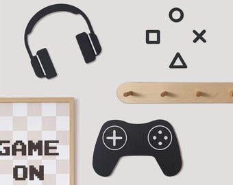 May include: Black and white wall decor with a game theme. The decor includes a pair of headphones, a game controller, a square, a circle, an X, a triangle, and a wooden coat rack with five hooks. The text "GAME ON" is printed on a white and black checkered background.