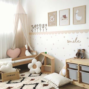 May include: A white canopy bed with a pink heart-shaped pillow and a wooden storage box. The wall behind the bed is decorated with a floral border, a row of stars, and the word "smile". There are three framed pictures on the wall, one with a flower, one with a house, and one with a goose.
