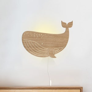 May include: A wooden whale-shaped night light with a white cord. The whale is light brown and has a white outline of its body and tail.