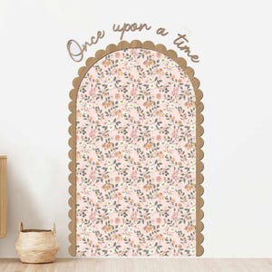 May include: A decorative wall arch with a scalloped wooden frame and a floral patterned interior. The pink background is covered in white, tan, and green floral designs. The words "Once upon a time" are above the arch.