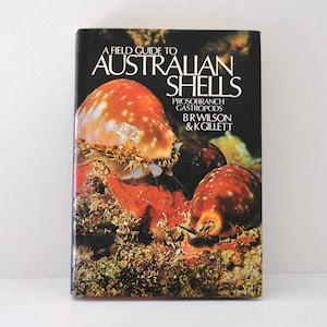 May include: A hardback book titled A Field Guide to Australian Shells: Prosobranch Gastropods by B R Wilson & K Gillett. The black cover features a colour photograph of two sea snails on a textured, rocky, and coral-covered ocean floor.