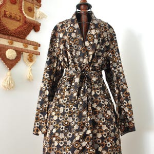 May include: A long, black floral print robe with a tie waist. The robe features a repeating pattern of white, grey, and orange flower-like shapes. The robe is displayed on a wooden dress form.