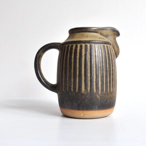 May include: A ceramic jug with a dark brown and tan vertical striped design. The jug has a handle and a spout. The base is a light orange colour. The jug is likely used for serving beverages.