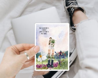 May include: A watercolor illustration of a person standing in a field of flowers. The person is holding a bouquet of flowers and is wearing a white dress and black boots. The text "May you be kind to yourself when you start to feel small" is written in black text on a white background.