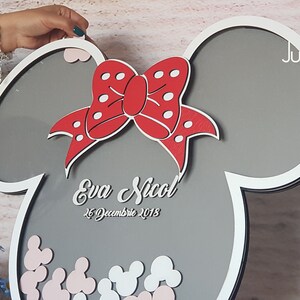 May include: A gray and white wooden frame shaped like Mickey Mouse ears with a red bow and white polka dots. The frame has a gray background with the text "Eva Nicol" and "26 Decembrie 2018" written in white. The frame is filled with small white and pink Mickey Mouse ears.
