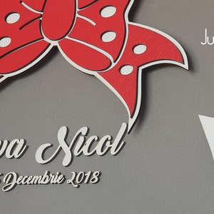 May include: A gray wooden frame with a white border and a red bow with white polka dots. The frame has a cutout in the shape of a cloud with the text "Eva Nicol" and "26 Decembre 2018" written in white. The frame is from Jubilee Frame, created with you.