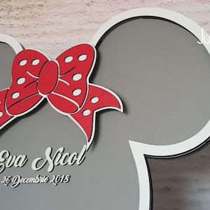 May include: A gray and white wooden cutout of a Mickey Mouse head with a red bow with white polka dots. The cutout has the text "Eva Nicol" and "26 December 2018" written on it.