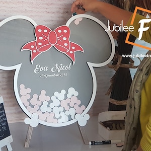 May include: A gray wooden Mickey Mouse shaped sign with a red bow and white polka dots. The sign says "Eva Nicol 26 December 2015" and has a space for guests to leave their well wishes.