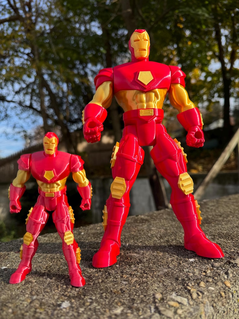 Puede incluir: Dos figuras de acci&oacute;n de Iron Man rojas y doradas. La figura m&aacute;s grande est&aacute; de pie con los brazos extendidos, mientras que la figura m&aacute;s peque&ntilde;a est&aacute; de pie con los brazos a los lados. Ambas figuras tienen un acabado met&aacute;lico.
