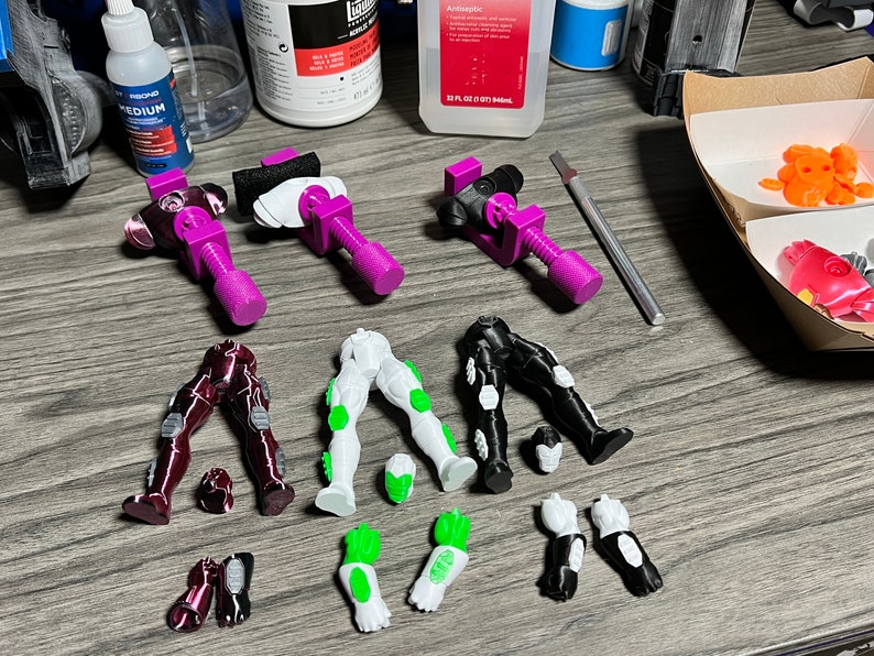 Puede incluir: Piezas de figuras de acci&oacute;n de pl&aacute;stico en colores rojo, blanco y negro. Las piezas incluyen piernas, brazos y manos. Las piezas est&aacute;n dispuestas sobre una superficie de madera.