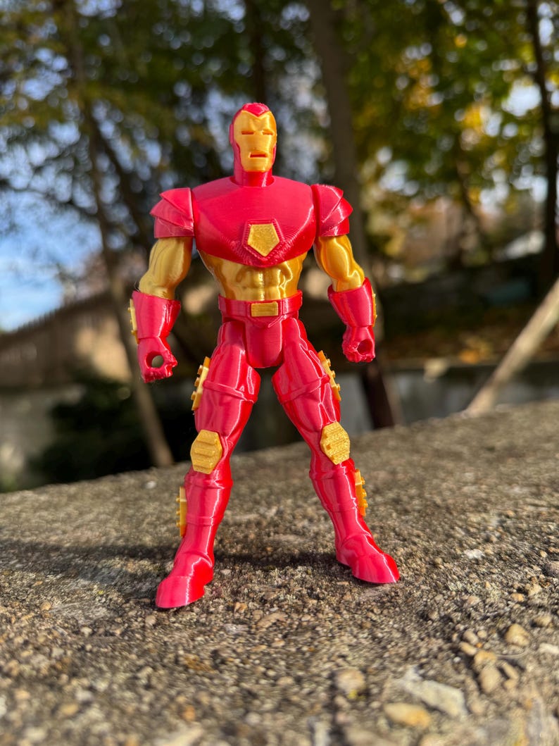 Puede incluir: Una figura de acci&oacute;n de Iron Man roja y dorada con un dise&ntilde;o detallado. La figura est&aacute; de pie sobre una superficie texturizada.