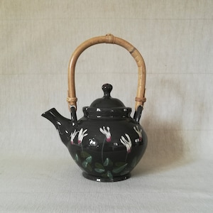 May include: A black ceramic teapot with a bamboo handle and white floral design. The teapot has a lid and a spout.