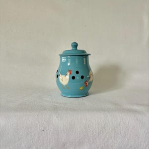 May include: A turquoise ceramic jar with a lid, decorated with white chickens, red combs, and black polka dots. The jar is round with a small knob on the lid. A decorative kitchen storage item, perfect for storing dry goods.