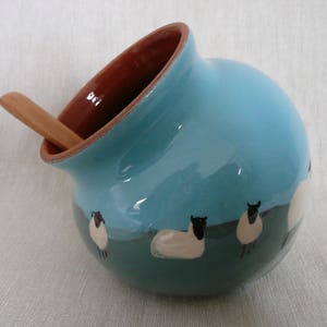 May include: A blue ceramic sugar bowl with a wooden spoon and a design of white sheep with black faces.