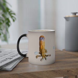 Peut inclure: Une tasse magique noire et blanche avec une pieuvre jaune aux yeux bleus et une coquille blanche sur un fond beige. La tasse porte l'inscription "Magic"