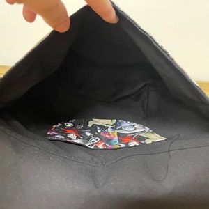 Puede incluir: Bolso tote de tela negro con un forro estampado en blanco y negro. El forro presenta una variedad de personajes y dise&ntilde;os.