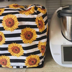 May include: A black and white striped cover featuring large yellow sunflowers with brown centers. The cover is next to a white kitchen appliance with a digital display and the word "VORWERK" printed on it.