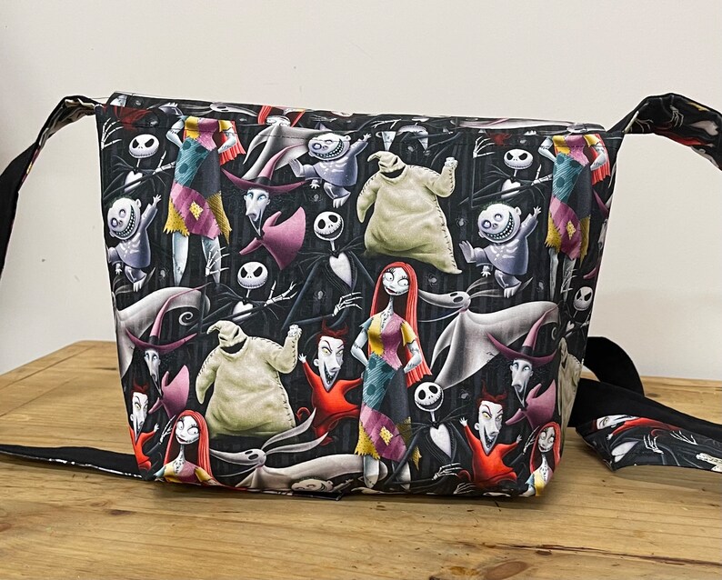 Puede incluir: Bolso de mano negro y blanco con tem&aacute;tica de Pesadilla Antes de Navidad con una variedad de personajes que incluyen a Jack Skellington, Sally y Oogie Boogie.