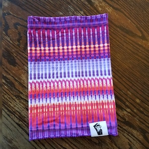 May include: A purple, pink, and orange patterned neck gaiter with a small black and white logo of a monkey wearing a hat.