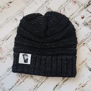 May include: Black knit beanie with a small white patch featuring a cartoon monkey wearing a top hat and bow tie.