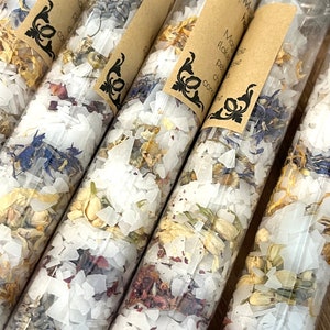 Puede incluir: Cinco tubos de vidrio transparente llenos de sales de ba&ntilde;o blancas y p&eacute;talos de flores secas. Los tubos tienen etiquetas de papel marr&oacute;n con texto negro que dice "Miracle Flake Bath Salts".