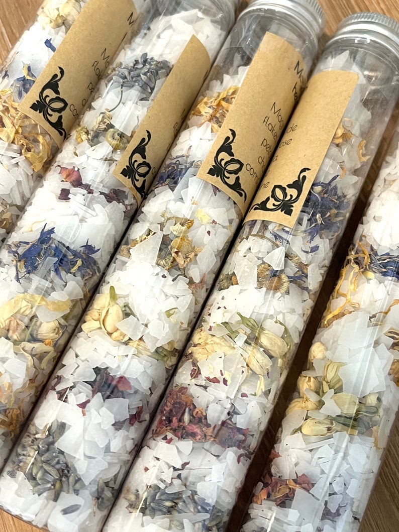 Puede incluir: Cinco tubos de vidrio transparente llenos de sales de ba&ntilde;o blancas y p&eacute;talos de flores secas. Los tubos tienen etiquetas de papel marr&oacute;n con texto negro que dice "Miracle Flake Bath Salts".