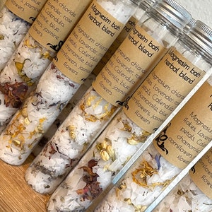 Puede incluir: Seis tubos de vidrio llenos de sales de ba&ntilde;o blancas y p&eacute;talos de flores secas. Los tubos est&aacute;n etiquetados "Magnesium Bath Herbal Blend" y enumeran los ingredientes: cloruro de magnesio, lavanda, p&eacute;talos de rosa, cal&eacute;ndula, manzanilla, aciano azul y flores de jazm&iacute;n.