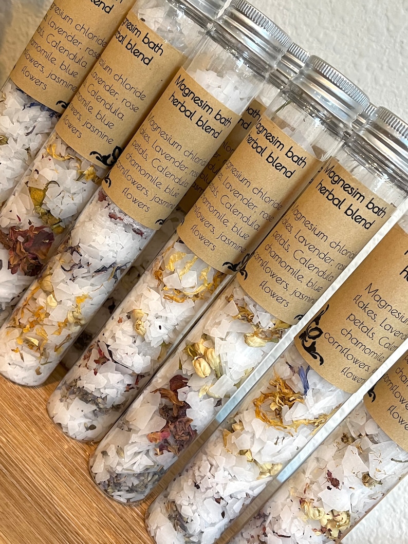 Puede incluir: Seis tubos de vidrio llenos de sales de ba&ntilde;o blancas y p&eacute;talos de flores secas. Los tubos est&aacute;n etiquetados "Magnesium Bath Herbal Blend" y enumeran los ingredientes: cloruro de magnesio, lavanda, p&eacute;talos de rosa, cal&eacute;ndula, manzanilla, aciano azul y flores de jazm&iacute;n.
