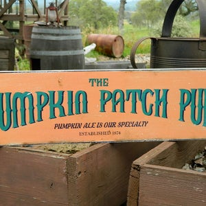 May include: A wooden sign with orange background and green text reads "The Pumpkin Patch Pub" with the tagline "Pumpkin Ale is our specialty" and "Established 1874".