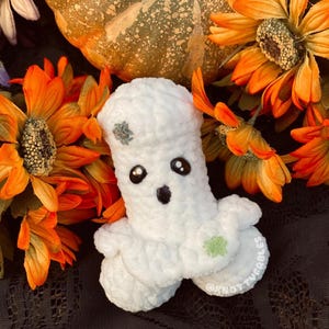 Peut inclure: Peluche fant&ocirc;me en crochet blanc avec des yeux noirs et une bouche noire. Le fant&ocirc;me a des d&eacute;tails brod&eacute;s verts sur sa t&ecirc;te et son corps. Le jouet est assis sur un fond de tournesols orange et une citrouille.