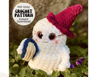Puede incluir: Un patrón de crochet para una figura fantasmal blanca que lleva un sombrero burdeos y sostiene un objeto azul y blanco. El texto "PAIGE Crochet Pattern" está en la parte superior. También están las palabras "Bookish Ghoul". El patrón está disponible como descarga PDF.