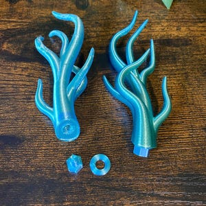 Peut inclure: Deux sculptures en forme d'arbre de couleur teal avec de multiples branches incurv&eacute;es. Les sculptures sont imprim&eacute;es en 3D et pr&eacute;sentent un effet d&eacute;grad&eacute;, passant du bleu au vert. Sont &eacute;galement inclus un petit cube et un anneau, tous deux de couleur teal assortie.