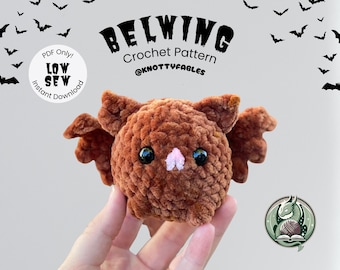 Op de afbeelding: Een bruin gehaakt vleermuisontwerp met zwarte ogen en een roze neus. De vleermuis heeft kleine vleugels. De afbeelding bevat de tekst "BELWING Crochet Pattern @knottyfables" en een logo met een draak en garen.