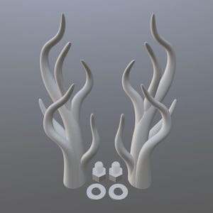 May include: Two white, abstract, horn-like sculptures with multiple curved branches. Two small, square-shaped objects and two circular objects are at the base of the sculptures. The background is a solid, light gray.