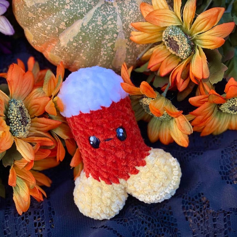 Peut inclure: Un jouet en peluche en forme de ma&iuml;s sucr&eacute; crochet&eacute; avec un dessus blanc, un milieu orange et un bas jaune. Le jouet a un visage mignon avec des yeux noirs et un petit sourire. Le jouet est entour&eacute; de fleurs orange et jaunes.