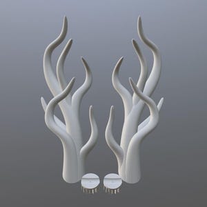May include: Two white, abstract sculptures resembling stylized antlers or branches. Each sculpture has multiple curved, upward-reaching forms. The bases have circular elements with small, peg-like details. The background is a solid, neutral gray.