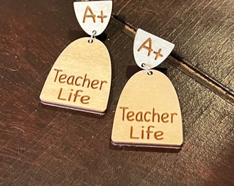 May include: A pair of wooden earrings with a silver charm that says "A+". The earrings are shaped like a teardrop and have the words "Teacher Life" engraved on them.