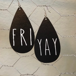 Puede incluir: Un par de pendientes de cuero negro en forma de l&aacute;grima con ganchos plateados. Los pendientes tienen las palabras "FRI" y "YAY" escritas en blanco.