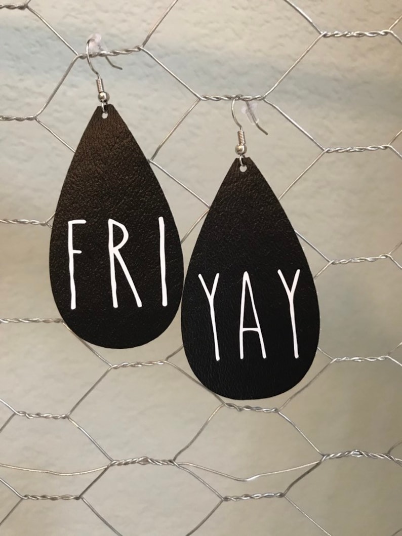Puede incluir: Un par de pendientes de cuero negro en forma de l&aacute;grima con ganchos plateados. Los pendientes tienen las palabras "FRI" y "YAY" escritas en blanco.