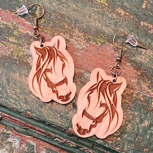 May include: A pair of wooden earrings featuring a horse head design. The earrings are brown and have a simple, elegant style.